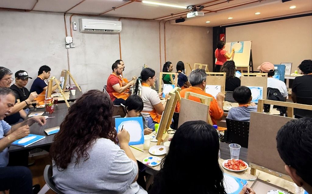 Salón lleno de alumnos y comunidad Sorda pintando en caballetes